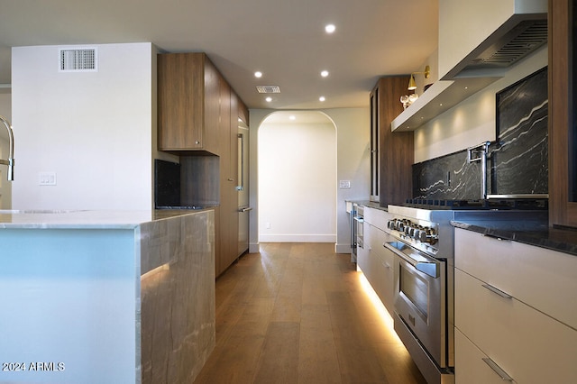 kitchen with high end range, dark wood-type flooring, dark stone counters, and tasteful backsplash