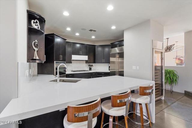 kitchen featuring kitchen peninsula, sink, a kitchen bar, and built in refrigerator