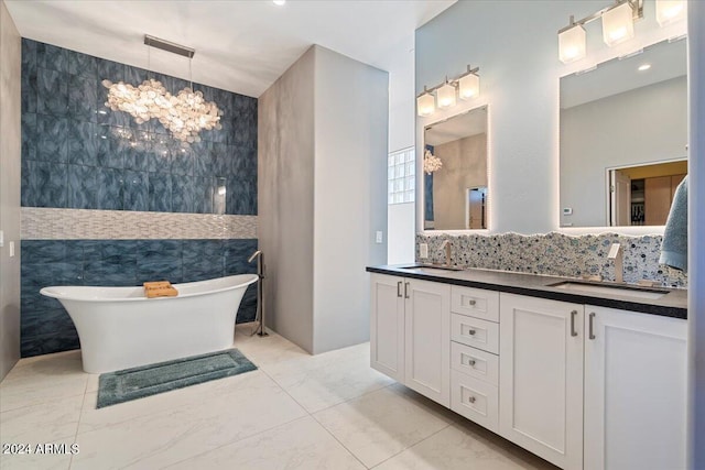 bathroom with vanity, an inviting chandelier, a tub to relax in, and tile walls