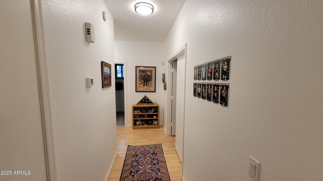 hallway with light wood finished floors and a textured wall