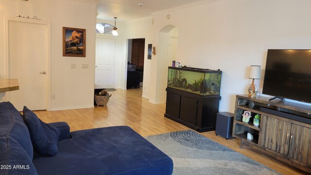 living room featuring arched walkways, baseboards, ornamental molding, and light wood-style floors