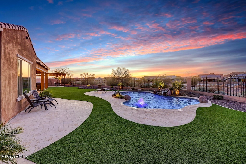 pool at dusk featuring pool water feature, a yard, and a patio