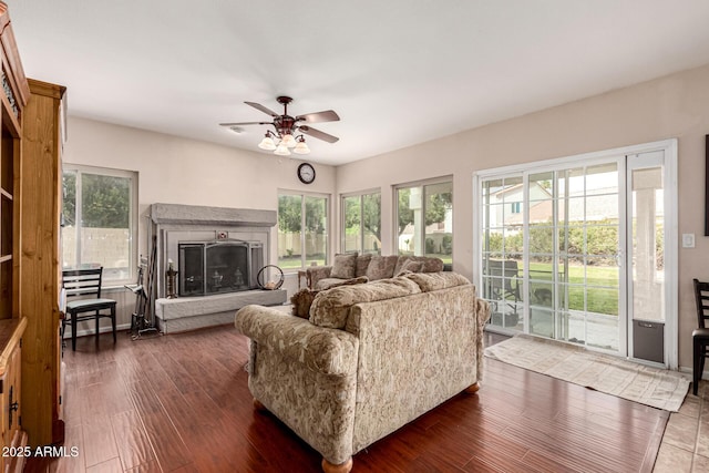 living area with dark wood-style floors, a fireplace with raised hearth, and a ceiling fan