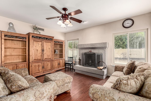 living room featuring dark wood-style floors, a fireplace with raised hearth, and ceiling fan