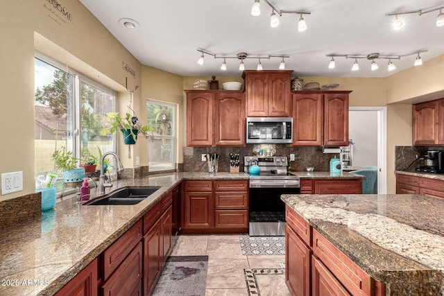kitchen featuring stainless steel appliances, backsplash, a sink, light stone counters, and brown cabinets
