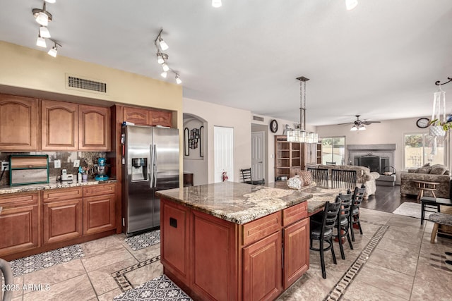kitchen featuring visible vents, a kitchen bar, arched walkways, stainless steel refrigerator with ice dispenser, and brown cabinetry