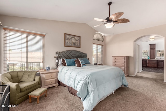 bedroom with connected bathroom, lofted ceiling, light colored carpet, arched walkways, and ceiling fan