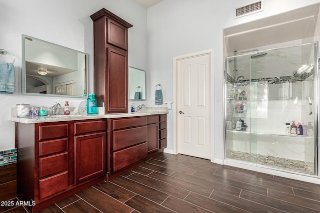 full bath with visible vents, double vanity, wood finish floors, a sink, and a stall shower