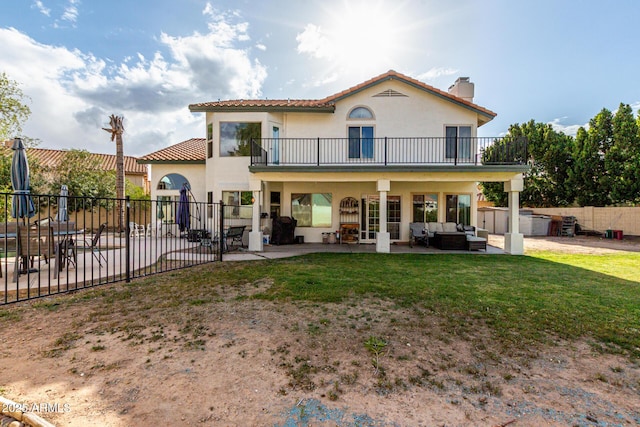 back of property with a balcony, fence, stucco siding, a lawn, and a patio area