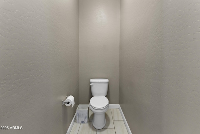 bathroom featuring tile patterned flooring, toilet, a textured wall, and baseboards