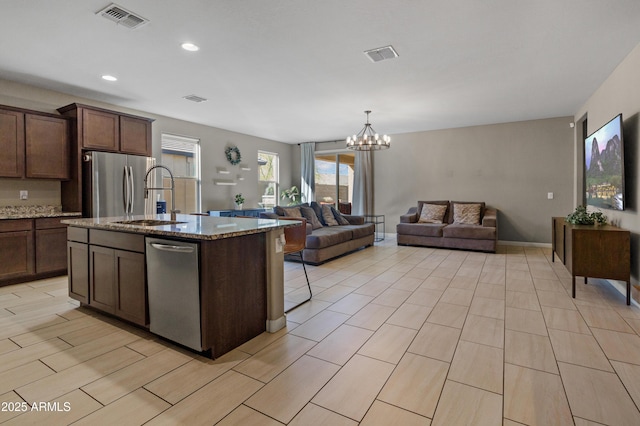 kitchen with visible vents, appliances with stainless steel finishes, open floor plan, light stone counters, and a sink