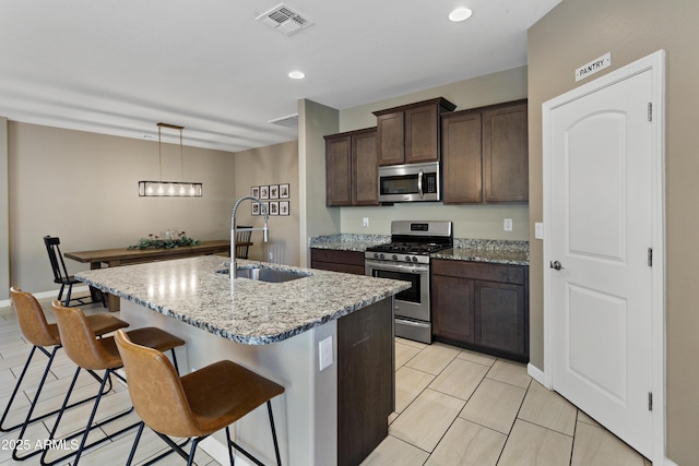 kitchen with visible vents, appliances with stainless steel finishes, light stone countertops, a kitchen island with sink, and a sink