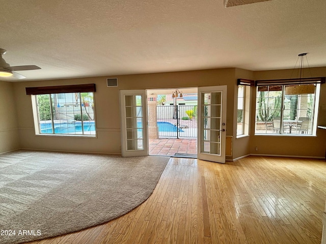 doorway to outside featuring ceiling fan with notable chandelier, light hardwood / wood-style flooring, and a textured ceiling