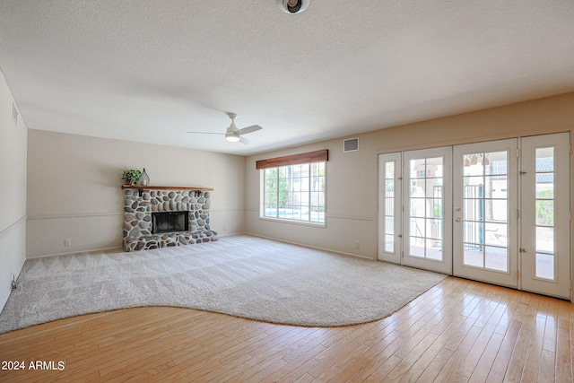 unfurnished living room with a fireplace, ceiling fan, light hardwood / wood-style floors, and a textured ceiling