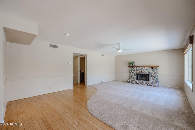 unfurnished living room featuring ceiling fan, light wood-type flooring, and a stone fireplace