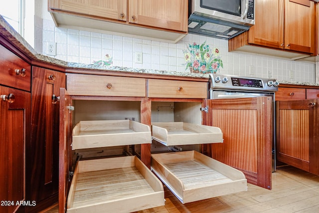 kitchen featuring appliances with stainless steel finishes, light hardwood / wood-style flooring, light stone counters, and decorative backsplash