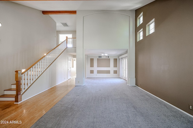 unfurnished living room featuring beamed ceiling, a towering ceiling, and hardwood / wood-style floors