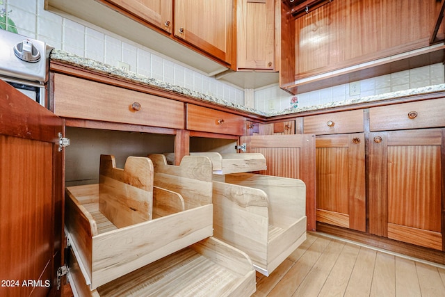 interior details with tasteful backsplash, light stone countertops, and light hardwood / wood-style floors