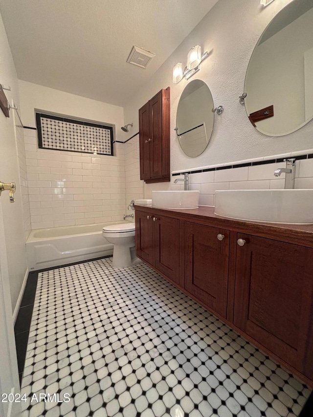 full bathroom featuring toilet, tiled shower / bath, tile walls, a textured ceiling, and vanity