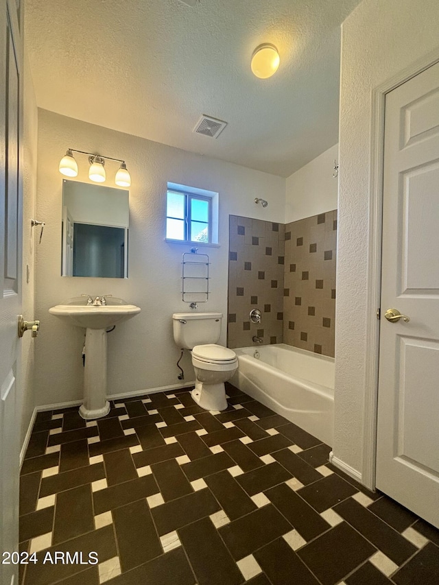 bathroom featuring tiled shower / bath, a textured ceiling, and toilet