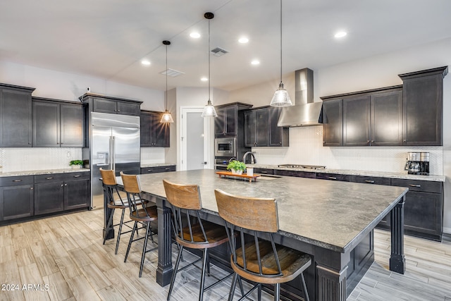 kitchen with a large island with sink, sink, a kitchen bar, wall chimney exhaust hood, and decorative light fixtures