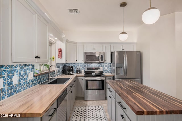 kitchen with backsplash, visible vents, appliances with stainless steel finishes, a sink, and butcher block counters
