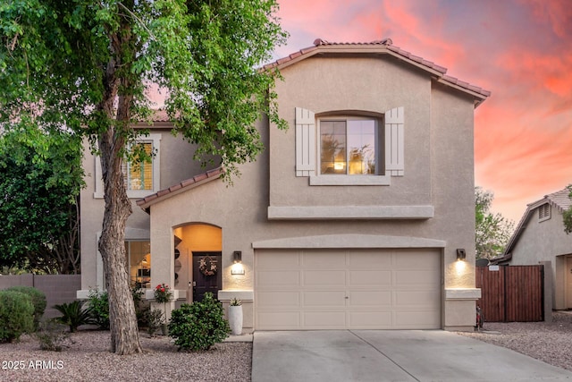 mediterranean / spanish home featuring an attached garage, stucco siding, a tile roof, and fence