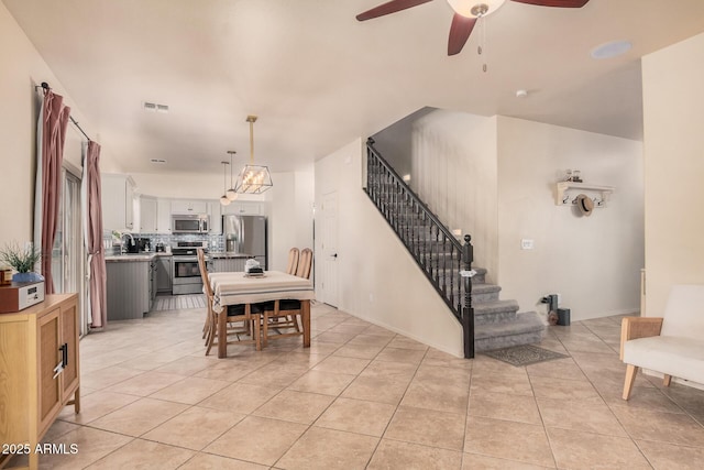 dining space featuring visible vents, a ceiling fan, light tile patterned floors, and stairway