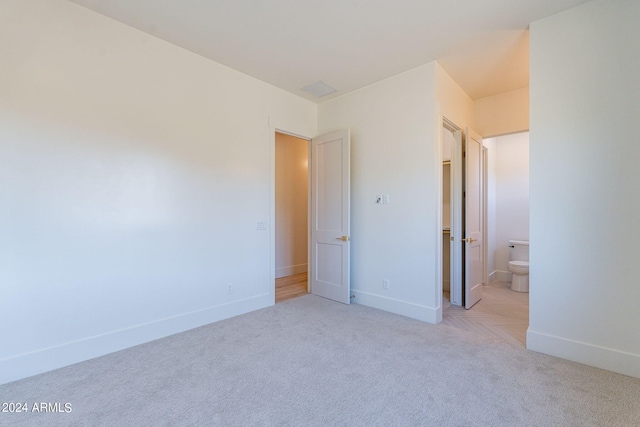 unfurnished bedroom featuring ensuite bathroom and light colored carpet