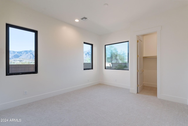 unfurnished bedroom featuring a mountain view, light carpet, a spacious closet, and a closet