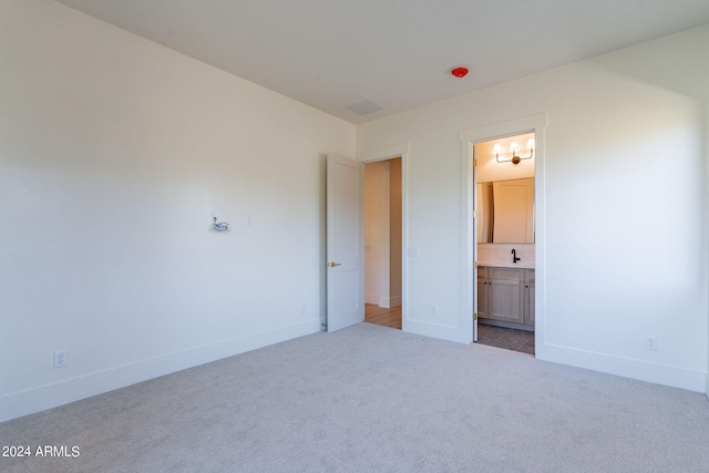 unfurnished bedroom with ensuite bath, sink, and light colored carpet