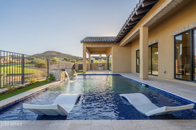 view of pool with a mountain view, pool water feature, an outdoor kitchen, and a patio