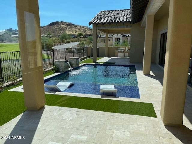 view of swimming pool with pool water feature, a mountain view, a patio area, and an outdoor kitchen