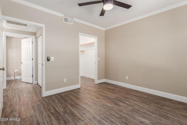 unfurnished bedroom with crown molding, wood-type flooring, a spacious closet, and ceiling fan