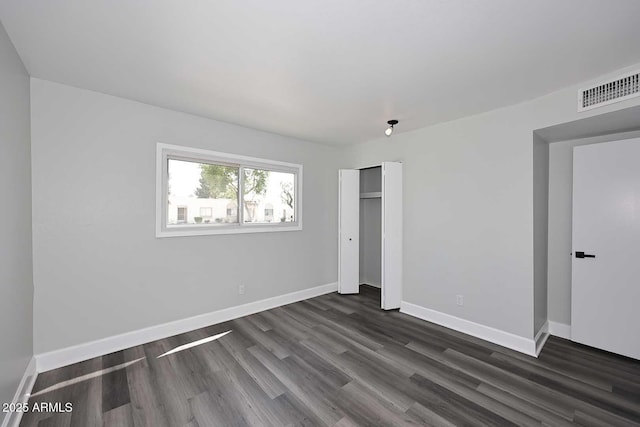 unfurnished bedroom with dark wood-style flooring, baseboards, visible vents, and a closet