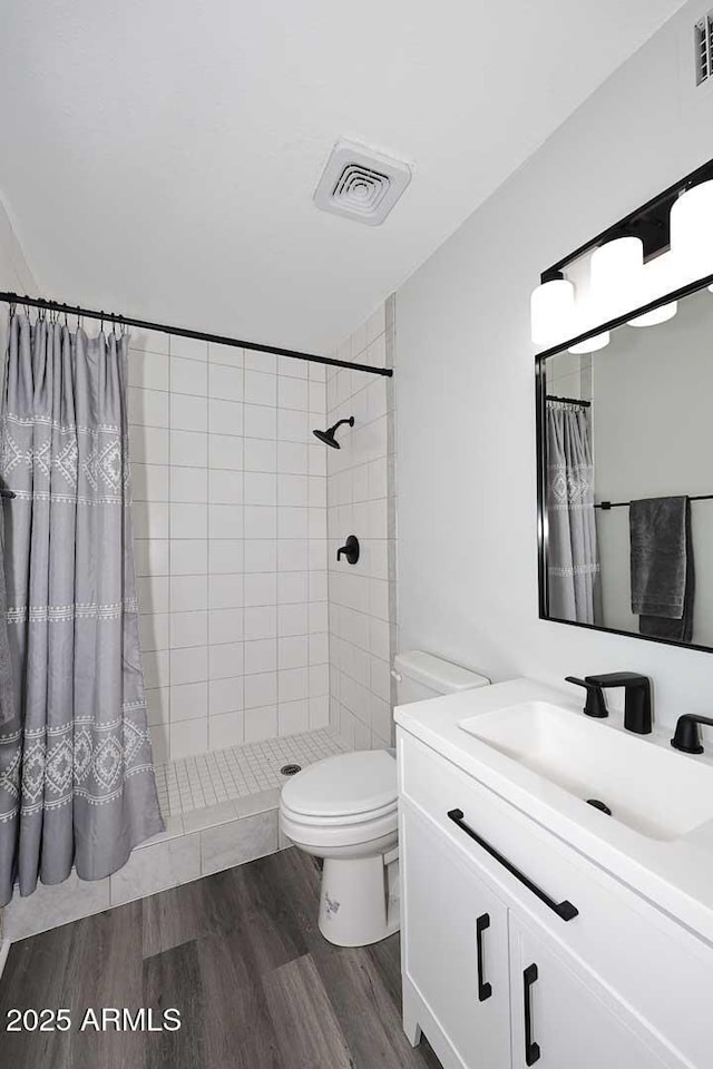 full bathroom featuring vanity, toilet, wood finished floors, visible vents, and tiled shower