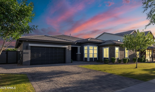 view of front facade featuring decorative driveway, a garage, stucco siding, and a yard