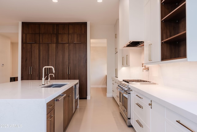 kitchen with decorative backsplash, white cabinetry, a sink, stainless steel stove, and wall chimney exhaust hood