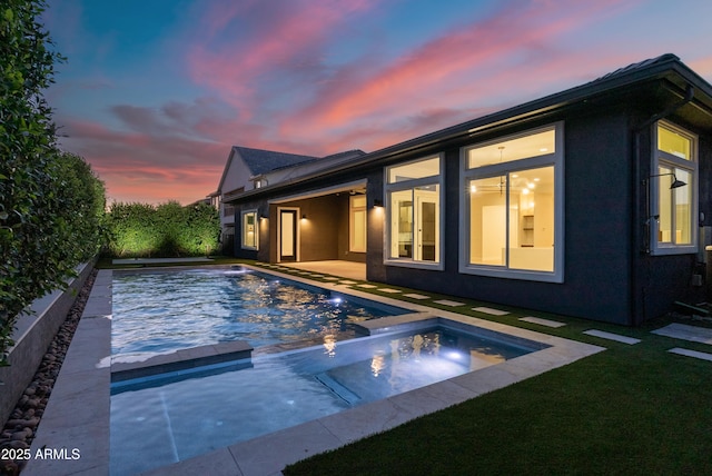 back of property at dusk with a pool with connected hot tub, a yard, and a patio area