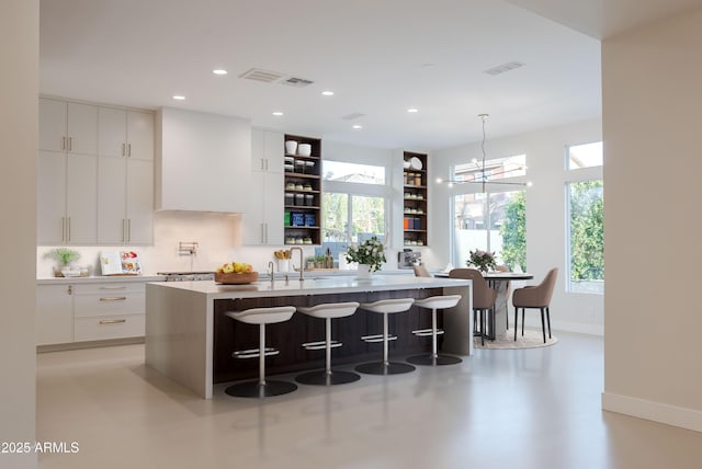 kitchen with open shelves, baseboards, an island with sink, a breakfast bar area, and modern cabinets