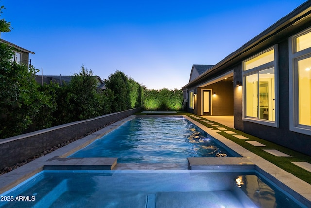 pool at dusk with a pool with connected hot tub