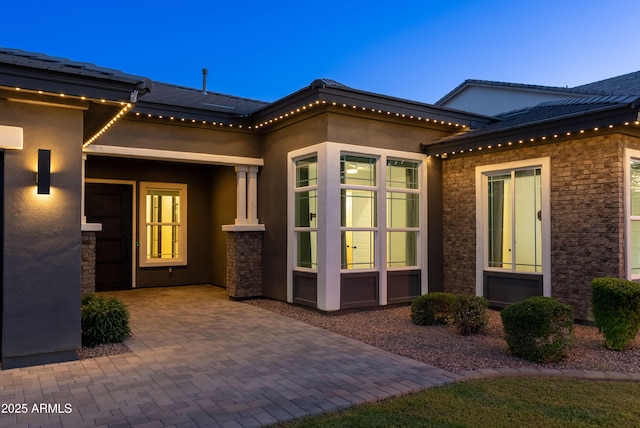 doorway to property with a patio area, stucco siding, and stone siding