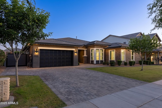 prairie-style home featuring a front yard, decorative driveway, stucco siding, an attached garage, and a tile roof