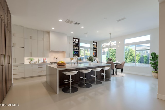 kitchen featuring white cabinets, baseboards, a kitchen bar, a center island with sink, and modern cabinets