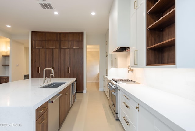 kitchen featuring open shelves, a center island with sink, a sink, white cabinets, and stainless steel appliances
