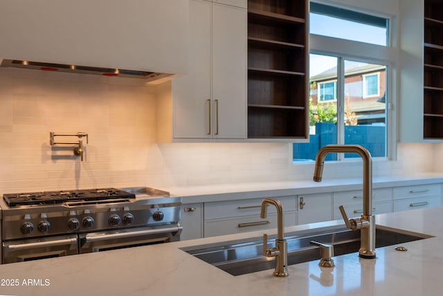 kitchen featuring range with two ovens, tasteful backsplash, open shelves, light stone countertops, and wall chimney exhaust hood
