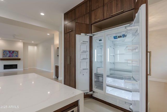 kitchen with dark brown cabinetry, modern cabinets, a fireplace, light stone countertops, and recessed lighting