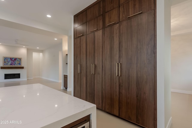 interior space featuring dark brown cabinets, a fireplace, modern cabinets, recessed lighting, and light stone counters