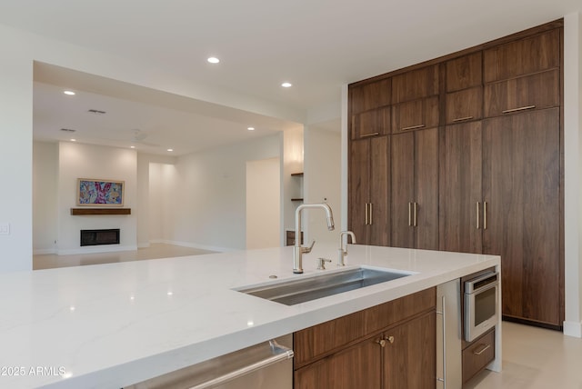kitchen featuring a fireplace, light stone countertops, a sink, open floor plan, and recessed lighting
