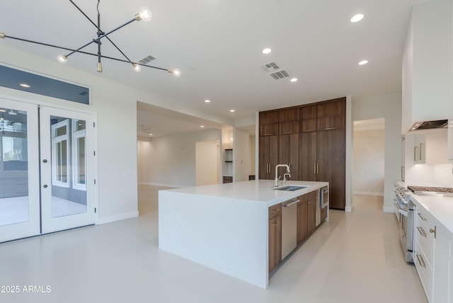 kitchen featuring appliances with stainless steel finishes, a sink, light countertops, visible vents, and a center island with sink